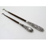 Two silver handled button hooks with embossed decoration.