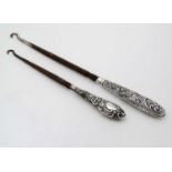 Two silver handled button hooks with embossed decoration.