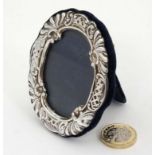 A silver photograph frame of oval form with embossed decoration and velvet easel / strut back .