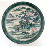 A green and white Japanese plate decorated with figures beside a river in a mountainous landscape,