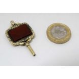 A yellow metal watch key set with hardstone carnelian to centre.