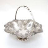 A silver plated pedestal cake basket with floral fruit and C-scroll decoration and swing handle.