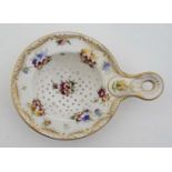 A 19thC Dresden style hand painted porcelain tea strainer decorated with flowers and having gilt