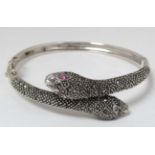 A silver bracelet / bangle formed as two snake heads with marcasite decoration and red stone eyes.