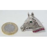 A silver brooch formed as a horses head set with red and green stones.