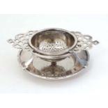 A silver plate tea strainer on stand.