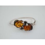 A Continental silver bracelet set with amber cabochon and foliate scrolls. Indistinctly marked.