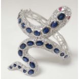 A silver bangle of snake form set with various blue sapphire coloured stones , with red stone eyes.