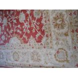 A LARGE INDIAN HANDMADE WOOLLEN CARPET worked with stylised foliate patterns against a pale red