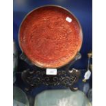 A CINNABAR LACQUER PLATE with all over carved decoration, on a wooden stand