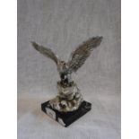 A SILVERED METAL SCULPTURE OF AN EAGLE with wings outstretched on a rocky outcrop