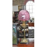 AN EDWARDIAN BRASS OIL LAMP, with a cranberry frosted shade