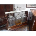 AN EDWARDIAN OAK THREE BOTTLE TANTALUS with silver plated mounts