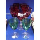 A SET OF SEVEN VICTORIAN CRANBERRY WINE GLASSES with clear slice-cut stems and one other similar