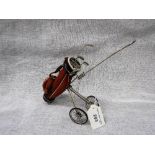 A WHITE METAL MINIATURE NOVELTY GOLF TROLLEY with leather bag and removable presentation golf clubs,