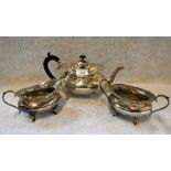 A GEORGE V THREE PIECE SILVER TEASET, the teapot with a scrolled ebony handle, all on raised paw