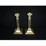 A PAIR OF BRASS CANDLESTICKS on a square foot with Corinthian column tops, 9" high