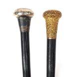 Two ebonised walking sticks one with gold plated pommel the other with a silver pommel, the