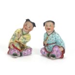 Pair of Chinese seated figures of children, both hand painted in the famille rose palette, the