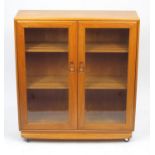 Ercol light elm book case fitted with a pair of glazed doors enclosing two adjustable shelves, label