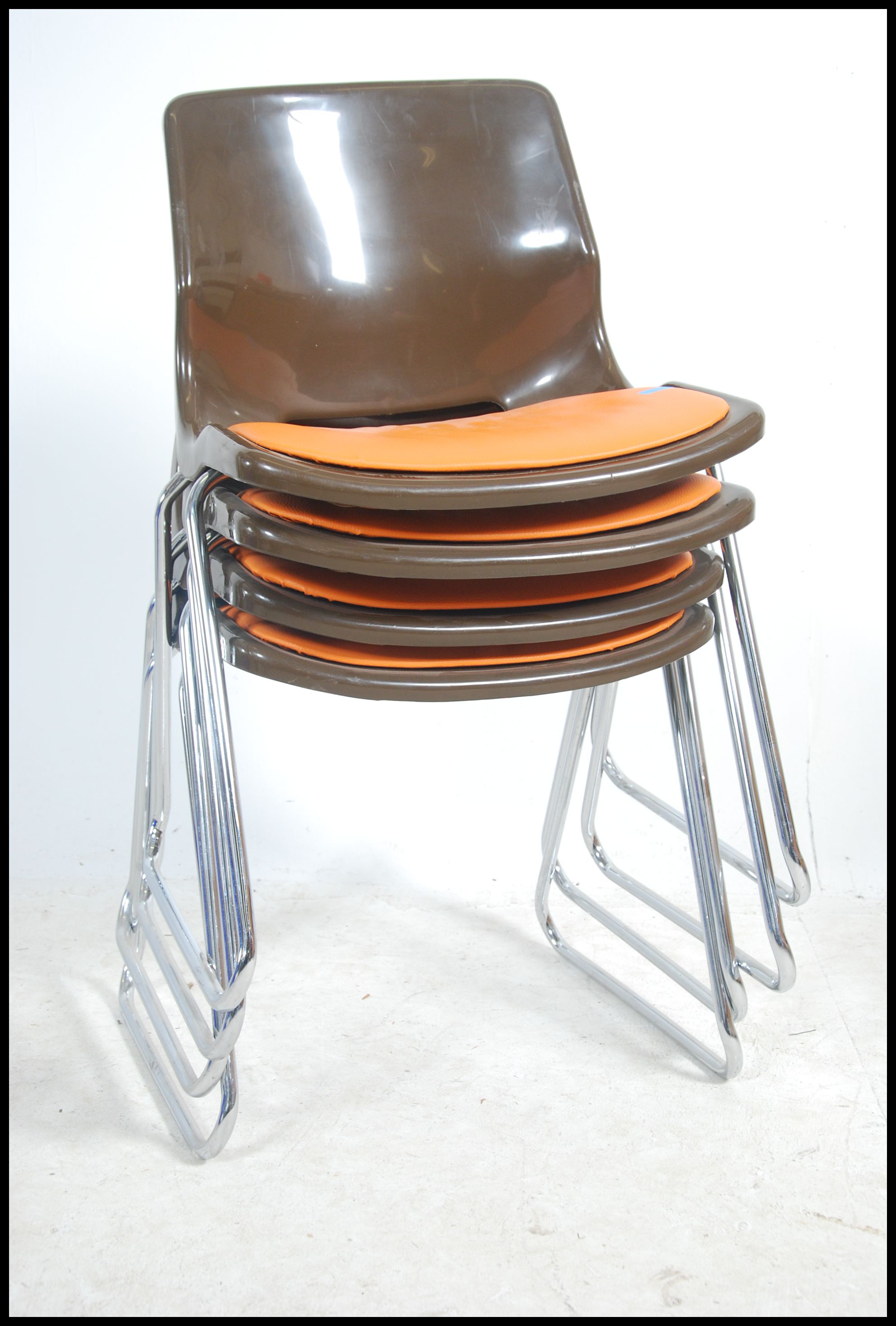 A set of 1970's retro stacking chairs in brown plastic having orange pad seats to the centre being