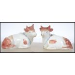 A pair of 19th century Staffordshire cow figurines. Each being seated having bells to neck.