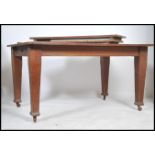 An Edwardian Arts & Crafts solid oak twin leaf wind out dining table being raised on squared legs