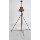 A vintage early 20th century wig stand raised on an adjustable tubular metal tripod base with wooden