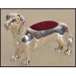 A large silver pin cushion in the form of a dog - dachshund hainv red baize lined cushion atop.