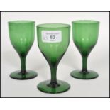 A trio of three 18th century Georgian Bristol green glass wine glasses each one raised on a plain