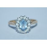 A hallmarked 9ct gold cluster ring set with a pale blue oval cut stone surrounded by a CZ halo.