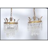 A pair of early 20th century Empire brass drop chandeliers having multiple faceted crystal drops.