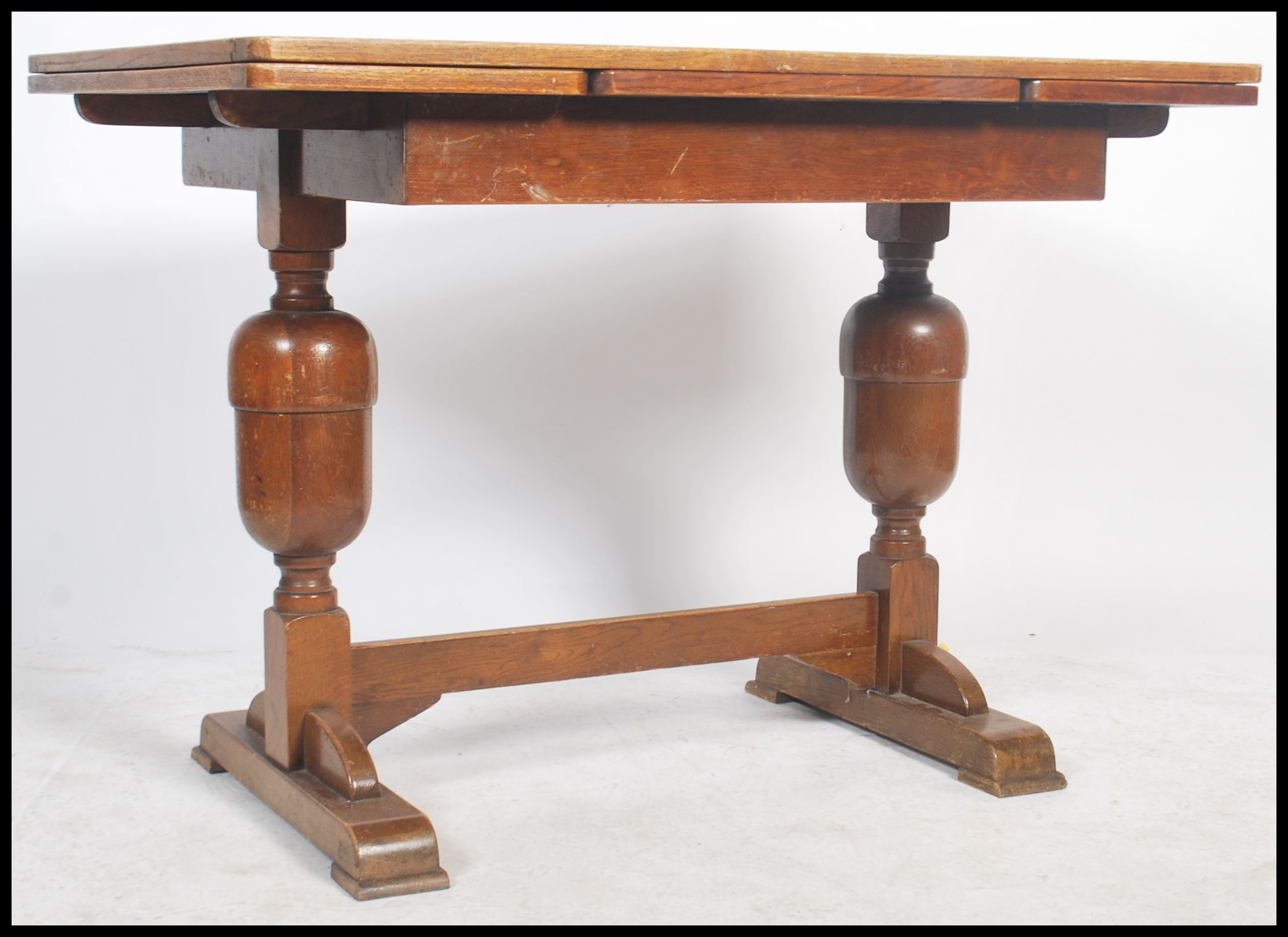 A 1930's oak draw leaf refectory dining table raised on turned legs united by stretcher having