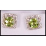 A pair of ladies silver, cz and peridot adorned earrings being cushion cut, each with halo's of cz'