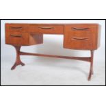 A 1970's G-Plan teak kneehole writing table desk raised on shaped supports with a series of drawers