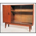 A vintage 1970's teak wood bookcase cabinet raised on tapered legs with a glass sliding door.