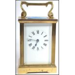 An early 20th century brass carriage clock with open escapement window and handle atop, ceramic face