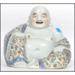 An Oriental ceramic large seated laughing Buddha decorated in famille rose patterned robes holding