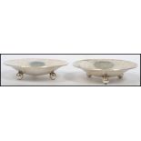 A pair of sterling silver pin dishes of concave circular form raised on three bun feet, makers