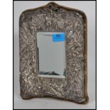 A silver easel mirror cast in relief with cherubs and putti with rococo scrollwork elsewhere. The