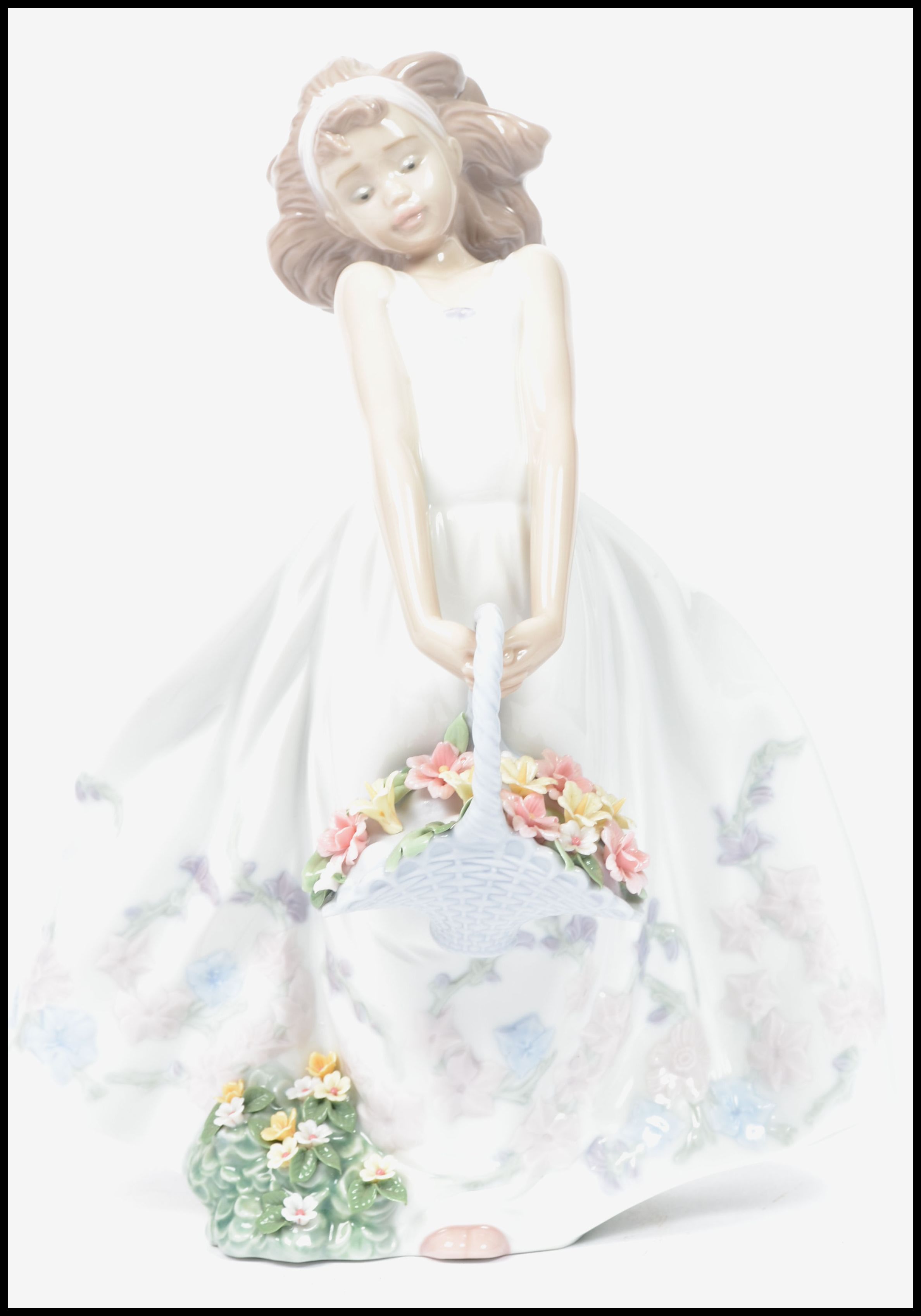 A Lladro ceramic figurine of a girl in dress holding a flower basket with floral bush to base.