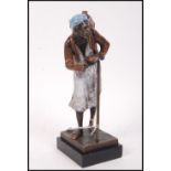 A cold painted bronze figurine of an Arab figure carrying water with bowl and cane raised on a