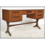 A 1970's G-Plan teak kneehole writing table desk raised on shaped supports with a series of