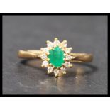 A hallmarked 18ct gold emerald and diamond cluster ring having a central oval cut emeralds