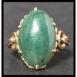 An 18k gold stamped vintage jade ring. Having a large jade cabochon with stylised shoulders. Stamped