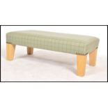 A contemporary upholstered beech wood footstool of rectangular form being upholstered in a green