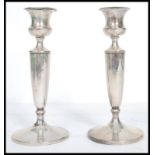 A silver hallmarked pair of candlesticks raised on terraced bases having tapering stems and single