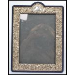 A silver hallmarked easel back picture frame having a bowed top with silver swirl and leaf