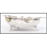 A vintage silver dish having a scalloped edge raised on tripod feet with central medallion depicting
