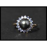 A 10ct gold and black pearl ring. The central black pearl having a halo of blue stones. Size S,